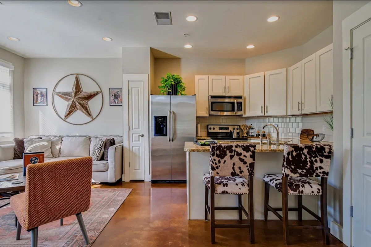 The image showcases a stylish open-concept living area highlighted by striking star wall decor, a plush sofa perfect for gatherings, and a modern kitchen with a spacious island and unique cowhide bar stools. The inviting setup hints at spaces where guests can cook, relax, and come together for memorable moments.