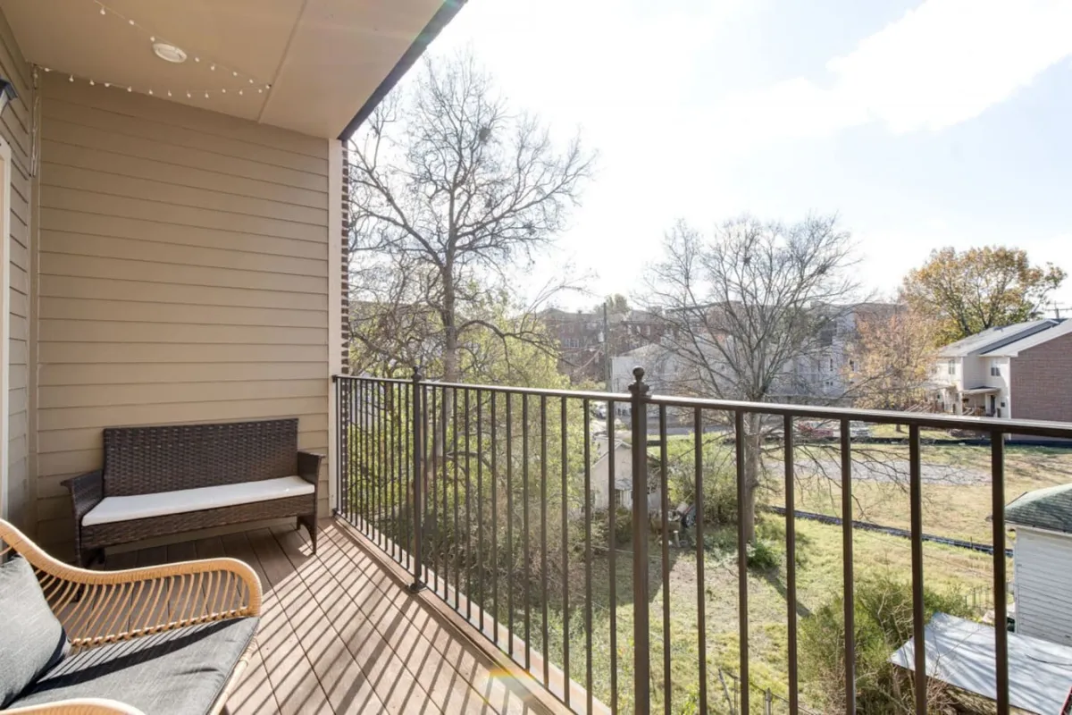 A serene exterior balcony featuring comfortable seating, a sturdy railing, and lush surrounding trees. The spacious outdoor area invites relaxation and offers a scenic spot to unwind, with enough room for families to gather and enjoy the view.