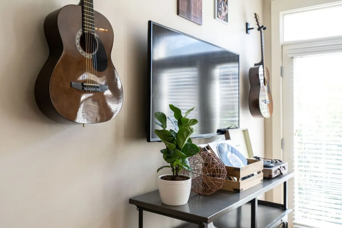 This image features a lounge area with guitars on the wall, a television, vinyl records, a decorative plant, and a basket. The scene evokes casual relaxation, music appreciation, and cozy group gatherings.
