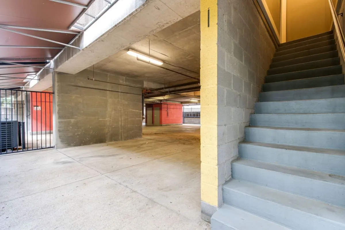 This image features a staircase leading from a practical, open space that serves as a transition area. Visible signs of daily activity such as parking vehicles and walking toward the upper levels are present, suggesting accessibility and the convenience of ground-level entry. The area is clean, well-lit, and ready for both arrival and departure, supporting the concept of secure, private parking and easy movement.